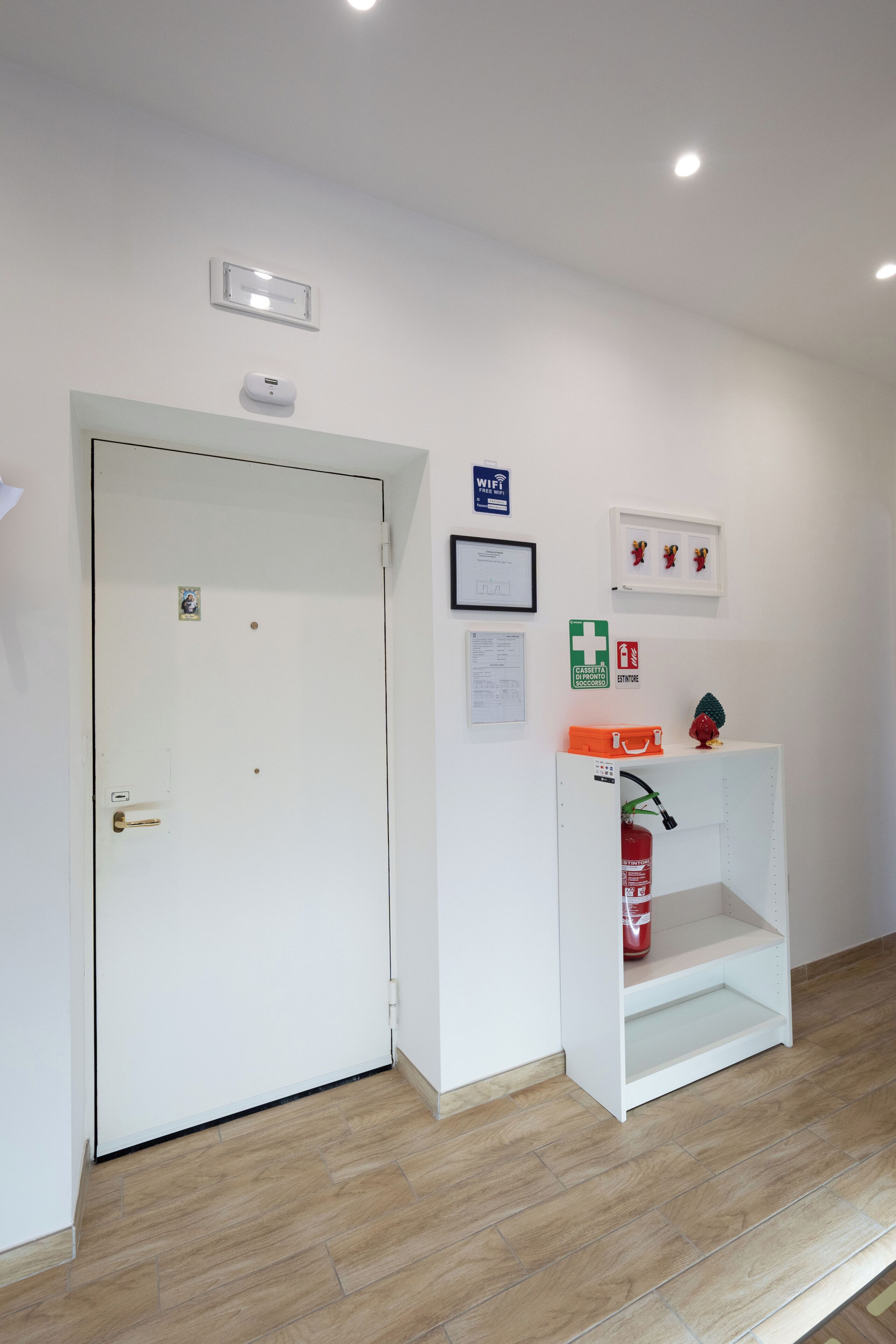A white door with a handle, a white shelf with a fire extinguisher, and a framed picture on the wall.
