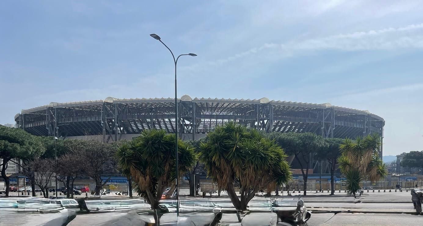 Een groot stadion met een overdekte tribune, omringd door bomen en lantaarnpalen.