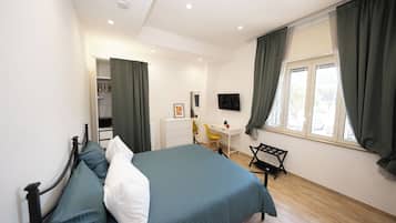Een slaapkamer met een bed, een bureau, een stoel, een televisie en een raam met gordijnen.