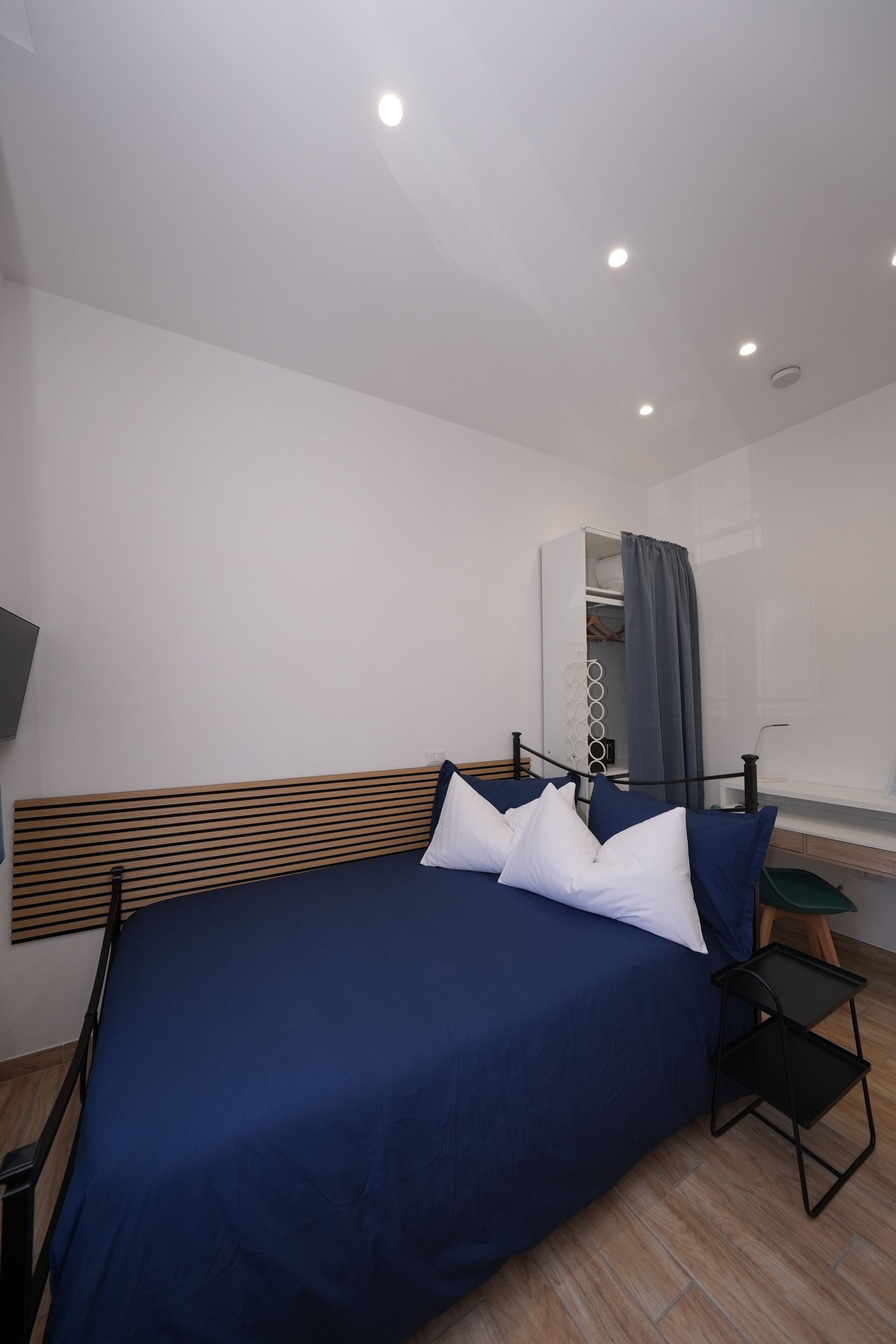 Een moderne hotelkamer met een houten hoofdbord, een bed met blauw beddengoed, een nachtkastje en een garderobe met spiegel.