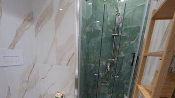 A bathroom with a marble wall, a glass-enclosed shower, a toilet, and a wooden shelf.