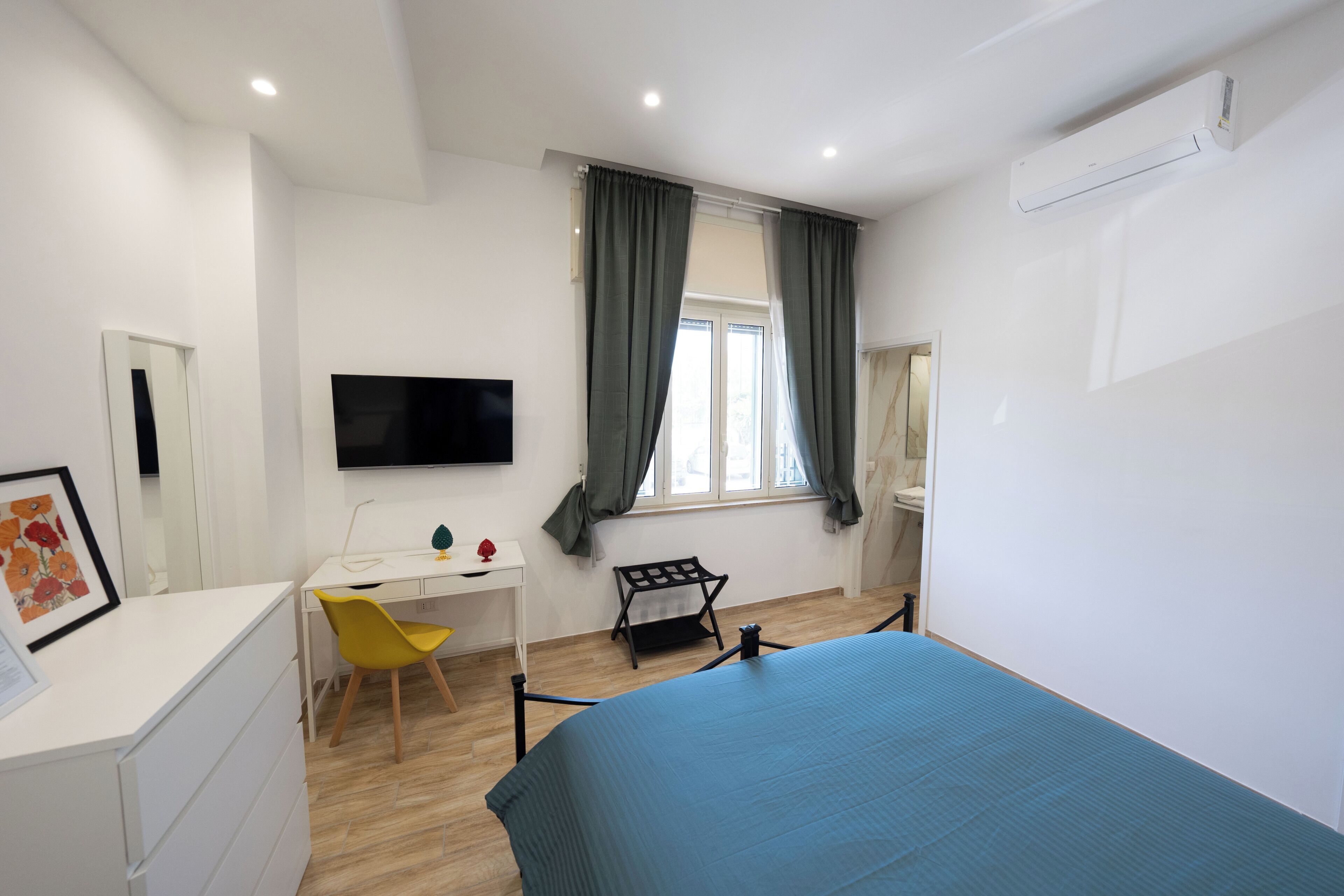A bedroom with a bed, a desk, a chair, a TV, and a window with curtains.
