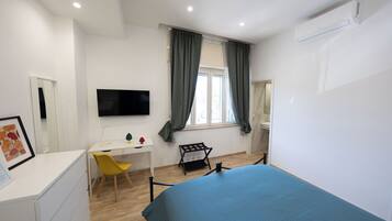 A bedroom with a bed, a desk, a chair, a TV, and a window with curtains.