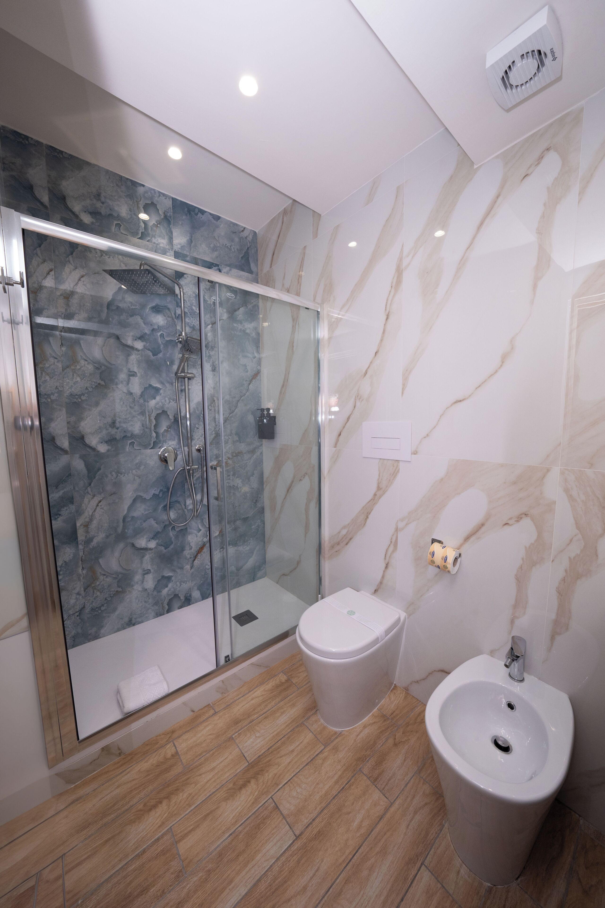 A modern bathroom with a glass-enclosed shower, a bidet, and marble walls.