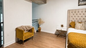 Un dormitorio con una cama, un sofá amarillo, un escritorio y un florero con plantas secas.