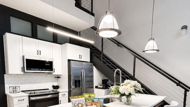 Cocina moderna con armarios blancos, electrodomésticos de acero inoxidable, una isla central con taburetes y luminarias colgantes.