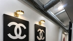 Un pasillo con dos grandes logotipos de Chanel negros montados en la pared, una pared blanca y un suelo de madera.