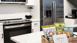 Una cocina con armarios blancos, electrodomésticos de acero inoxidable y una isla central con un cesto de aperitivos y una tarjeta de bienvenida.