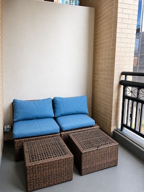 A balcony with a wicker sofa and ottomans, a brick wall, and a black railing.