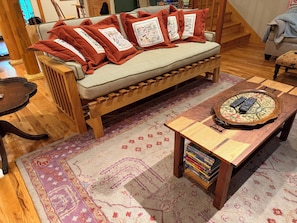 Un sofá de madera con cojines rojos, un banco a juego, una mesa de centro de madera con mandos a distancia y una alfombra estampada.