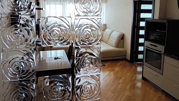 A modern kitchen with a wooden floor, a dining area with a table and chairs, a sofa, and a decorative glass partition with a rose pattern. - Cozy 2-Bedroom Apartment BIG Klaipeda (Klaipėda)