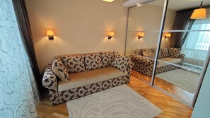 Une pièce comprenant un canapé, deux lampes fixées au mur, un grand miroir et un tapis à motifs.
