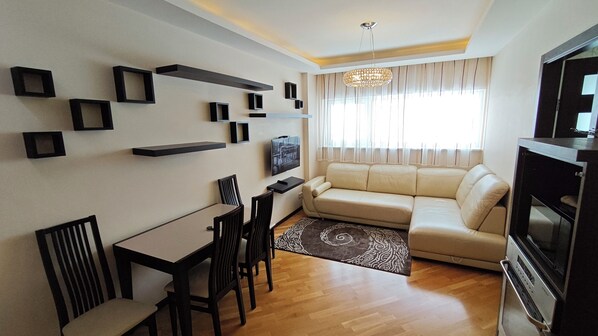 A living room with a sofa, TV, dining table, chairs, and decorative wall shelves.