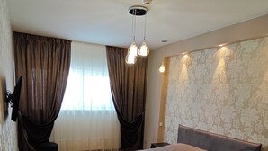 A modern bedroom with a large bed, a small side table, a chair, and a ceiling light fixture. - Cozy 2-Bedroom Apartment BIG Klaipeda (Klaipėda)