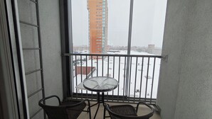 A balcony with a table and two chairs, overlooking a snowy cityscape with buildings. - Cozy 2-Bedroom Apartment BIG Klaipeda (Klaipėda)