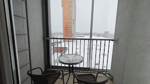Ein Balkon mit Tisch und zwei Stühlen, mit Blick auf eine verschneite Stadtlandschaft und Gebäude.