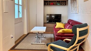 Ett vardagsrum med en röd soffa, en trästol, en tv och ett köksområde i bakgrunden.