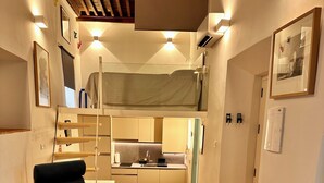 Ett kompakt bostadsutrymme med ett litet kök, en soffa, ett matbord och en våningssäng.