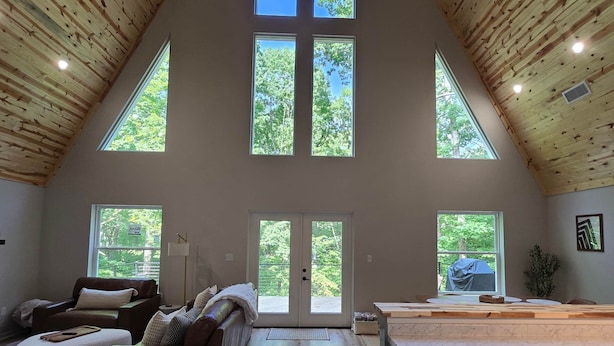 A spacious loft with a high ceiling, large windows, a cozy seating area, and a kitchen with a marble countertop. - The A at Elm Creek - Modern Cabin Retreat ~ Hot tub, Game loft, EV charger (Hot Spring County)