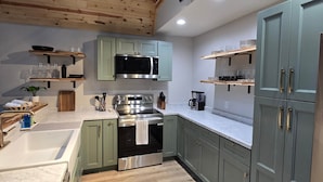 A modern kitchen with wooden ceiling beams, a stainless steel oven, and light green cabinets. - The A at Elm Creek - Modern Cabin Retreat ~ Hot tub, Game loft, EV charger (Hot Spring County)