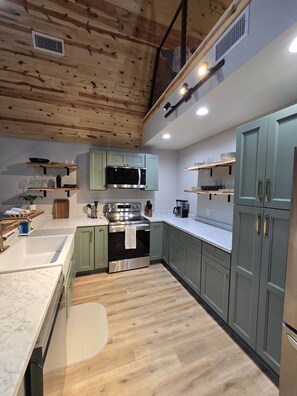 Eine moderne Küche mit Holzbalkendecke, einem Edelstahlbackofen und hellgrünen Schränken.