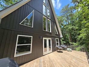 Ein modernes, zweistöckiges Haus mit großen Fenstern, einer Terrasse und Blick auf den umliegenden Wald.