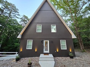 Ein dunkel gefärbtes Haus mit einem Satteldach, einer Haustür, zwei Fenstern im Erdgeschoss und einer kleinen Veranda.