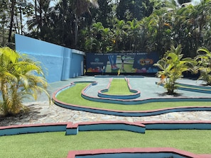 Ein Minigolfplatz mit blauer Wand und tropischen Pflanzen.