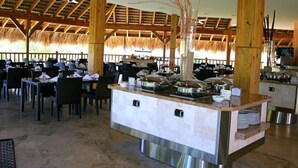 A buffet setup with multiple serving stations, a high ceiling with wooden beams, and a thatched roof in the background. - Lifestyle Holidays Vacation Club (Puerto Plata)