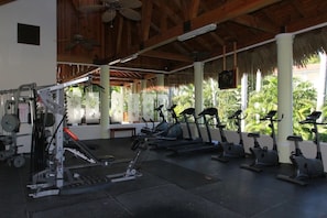 Una palestra con attrezzi da allenamento, un ventilatore a soffitto e vista su palme.