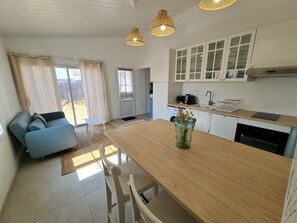 A modern kitchen with white cabinets, a dining table, and a blue sofa. - LA NOUVELLE VAGUE 100M FROM THE SEA (La Guérinière)