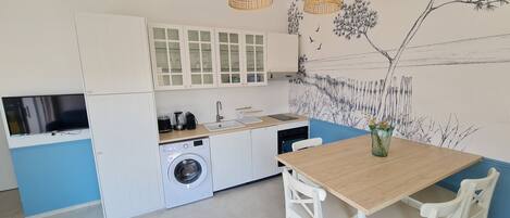 Cozinha moderna com máquina de lavar, pia e área de jantar com mesa e cadeiras.