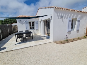 A white building with a tiled roof, a patio with a table and chairs, and a gravel driveway. - LA NOUVELLE VAGUE 100M FROM THE SEA (La Guérinière)