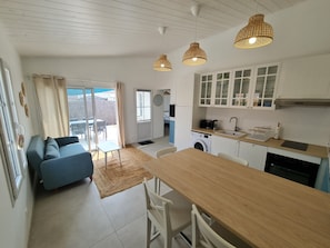 A modern kitchen with white cabinets, a wooden dining table, and a built-in washing machine. - LA NOUVELLE VAGUE 100M FROM THE SEA (La Guérinière)