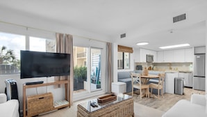 A modern living room with a flat-screen TV, a glass coffee table, and a dining area with a table and chairs. - Beachfront PCB 2BR Condo w Pools, Tennis & Gulf Views + Free Attraction Tix! (Panama City Beach)
