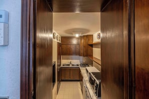 A narrow kitchen with wooden cabinets, a stove, and a microwave.