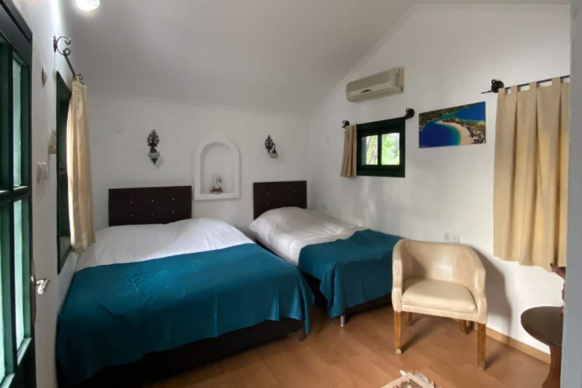 A room with two beds, a chair, a patterned rug, a painting, and a window with curtains.