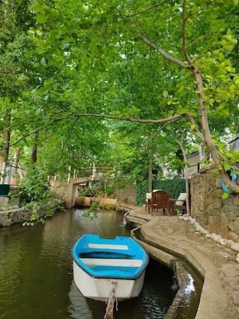 A serene waterway with a small boat docked at a stone bridge, surrounded by lush greenery.. Likya saklı bahçe