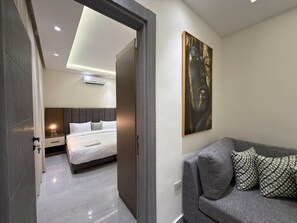 A modern hotel room with a bed, a sofa, a painting, and a door leading to another room. - 205 JRE Apartment in the Heart of Amman (Amman)