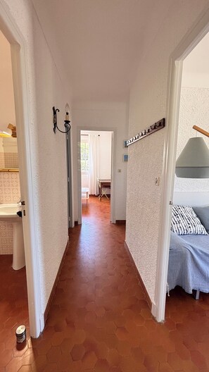 Ein Flur mit einem Bett, einem Sessel und einem Tisch im Hintergrund.