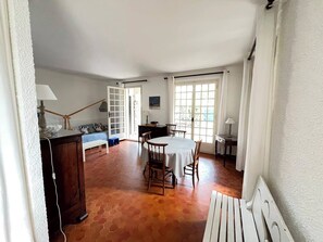 Ein Zimmer mit Esstisch, Stühlen, einer Bank, einer Couch und einem Fenster mit Vorhängen.