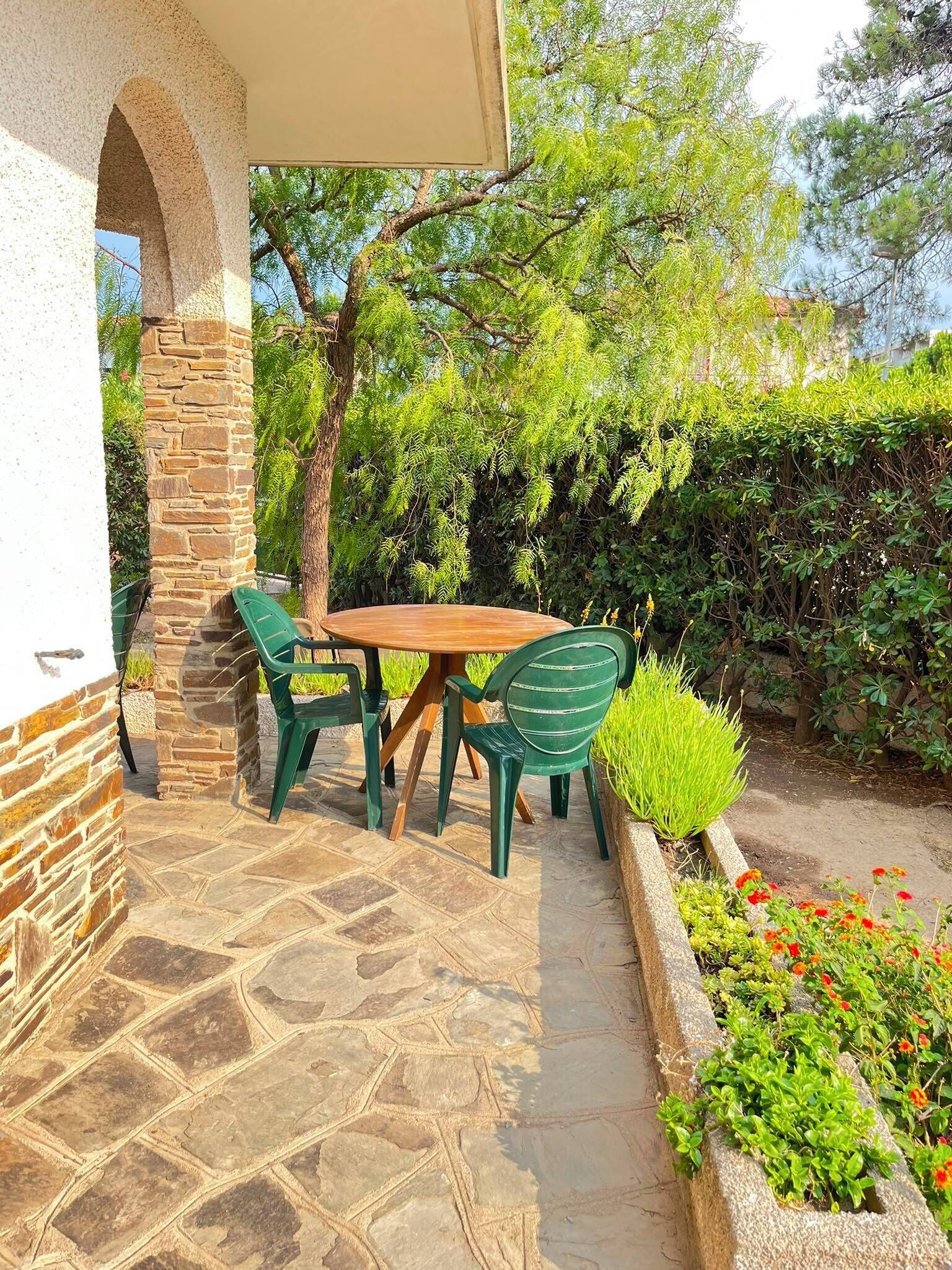 Une terrasse extérieure avec un sol en pierre, une table en bois et des chaises vertes.