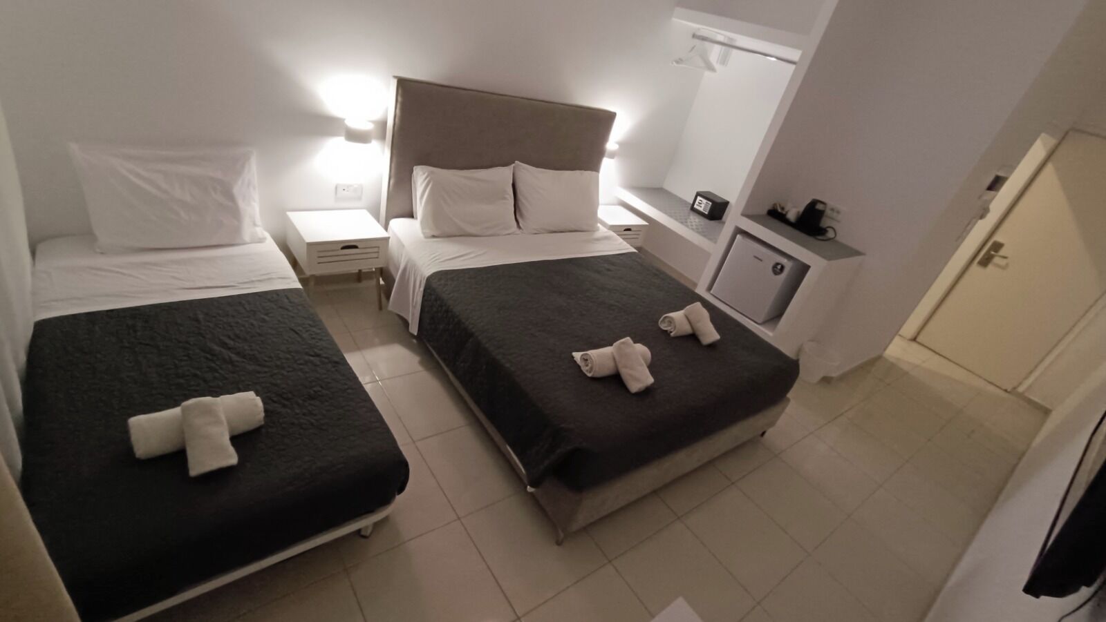 A hotel room with two beds, a nightstand, a bedside table, a small cabinet, and a door.