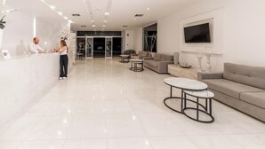 A modern hotel lobby with a reception desk, seating area, and a TV mounted on the wall. - Pefkos Breeze Family Resort & Spa (Rhodes)