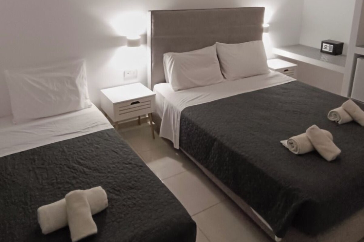 A hotel room with two beds, a bedside table, a nightstand, a mirror, and a ceiling light.