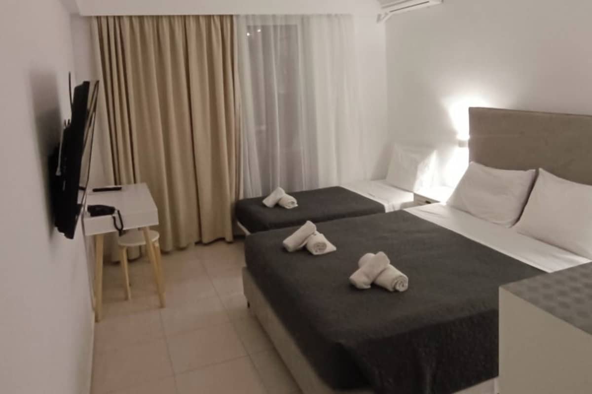 A hotel room with two beds, a desk, a chair, a TV, and an air conditioning unit.