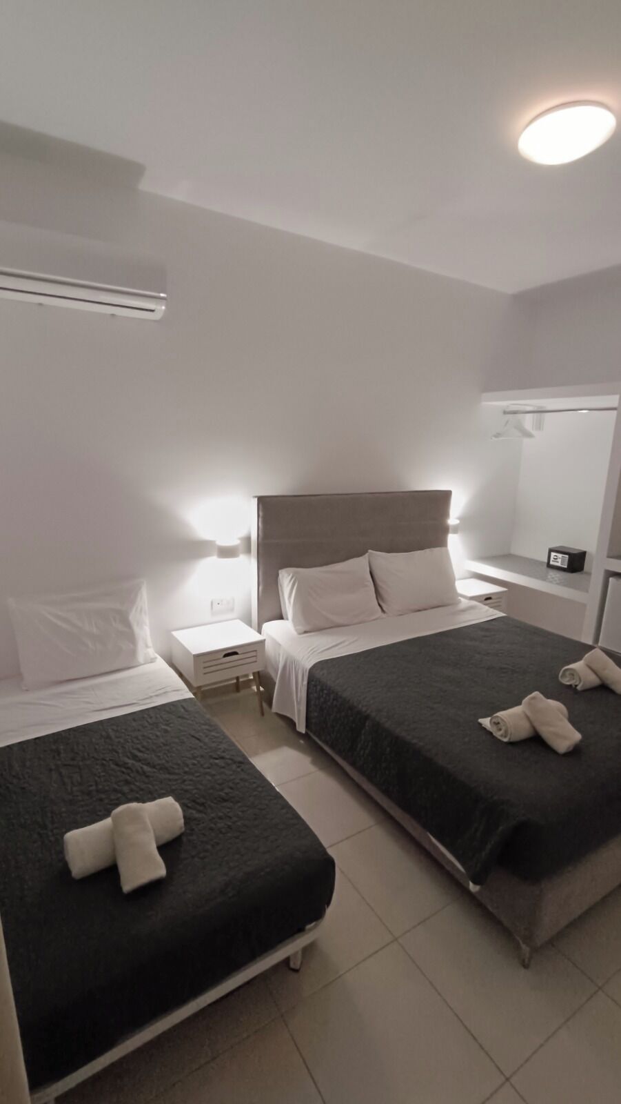 Habitación de hotel con dos camas, una mesita de noche, un espejo y una lámpara en el techo.