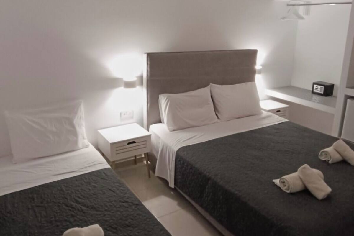 A hotel room with two beds, a bedside table, a nightstand, a mirror, and a ceiling light.