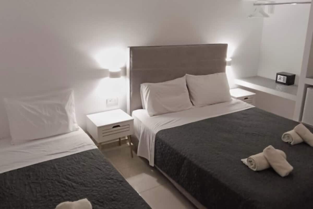A hotel room with two beds, a bedside table, a nightstand, a mirror, and a ceiling light.