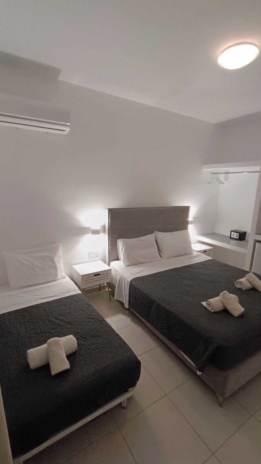 Habitación de hotel con dos camas, una mesita de noche, un espejo y una lámpara en el techo.